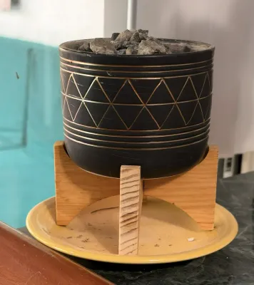 Modern black ceramic planter with etched gold geometric patterns, resting on a light wood stand and a yellow ceramic drip plate.