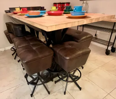 Industrial-style dining table with a thick butcher block top and black metal base, paired with matching brown tufted leather swivel...