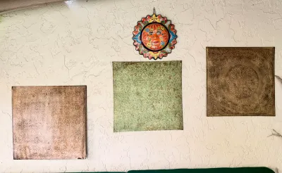 Trio of square embossed metal wall art panels with distressed finishes alongside a colorful Mexican Talavera ceramic sun face plaque.