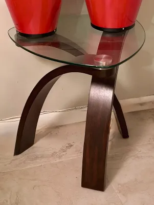 Contemporary end table featuring a triangular glass top supported by curved dark wood legs with silver metal hardware.