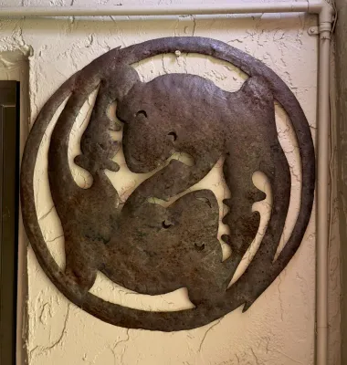 Circular rustic metal wall art featuring a stylized design of two interlocking geckos or lizards with a weathered, rusted patina.