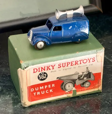 Vintage Dinky Toys blue loudspeaker van with paint wear, displayed on top of a Dinky Supertoys No. 562 Dumper Truck box showing some age...