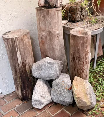 Assortment of natural landscaping elements, including three rustic wooden log pedestals of varying heights and four large decorative...