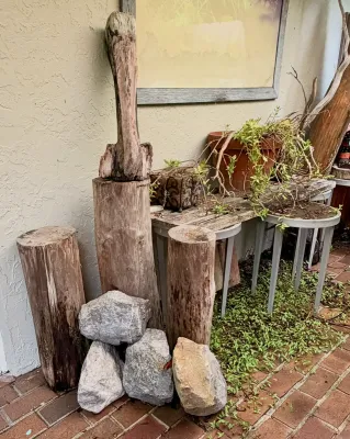 Rustic outdoor decor arrangement featuring weathered wood logs, natural stones, and potted plants on a wooden bench.