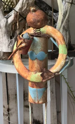 Whimsical rustic metal garden sculpture depicting a figure in a blue bikini holding a life preserver, showing weathered patina and rust.