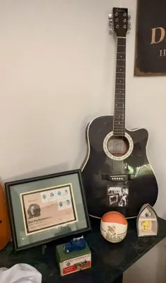 Black acoustic-electric cutaway guitar, shown alongside a framed Bob Marley commemorative stamp display, a vintage Dinky Supertoys box,...
