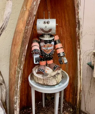 Handcrafted metal robot sculpture featuring a Harley-Davidson logo chest plate, standing on a wooden log slice base.