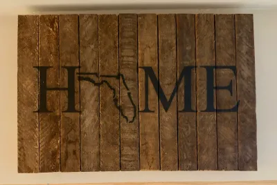 Rustic wooden wall art sign spelling "HOME" with the state of Florida replacing the letter "O", crafted from vertical...