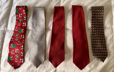 Collection of five men's neckties in various patterns, including a festive Santa Claus print, textured reds, and geometric designs.
