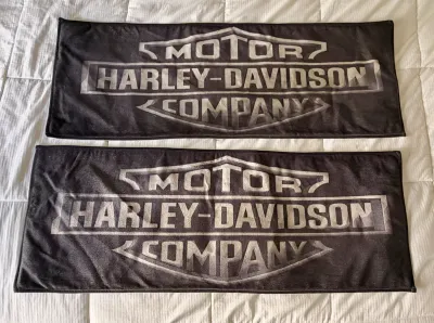 Pair of black Harley-Davidson Motor Company plush towels featuring the classic bar and shield logo in a distressed grey print.