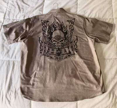 Harley-Davidson short-sleeve button-up shirt in a tan or light brown color, featuring a large back graphic with a flaming skull and...