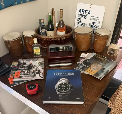 Eclectic tabletop display featuring vintage bongo drums, a basket of liquor bottles, a vintage Motorola brick cell phone, Harley-Davidson...