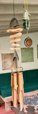 Handcrafted bamboo wind chime featuring a driftwood and painted coconut fish skeleton design, hanging alongside a green ceramic seahorse...
