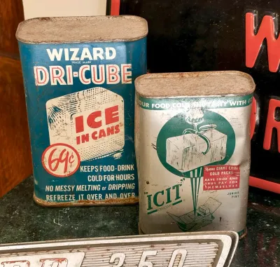Two vintage metal ice cans, including a blue Wizard Dri-Cube can and a silver and green Icit can, showing some rust and wear consistent...