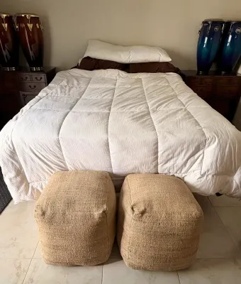 Pair of square woven jute pouf ottomans placed at the foot of a bed with a white comforter.