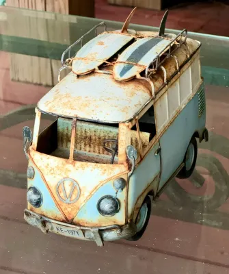 Vintage-style decorative metal model of a Volkswagen surfer van, featuring a distressed, rusted patina and two surfboards mounted on the...