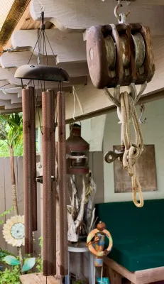 Vintage wooden triple-sheave block pulley with rope and a large bronze-finished metal wind chime hanging from patio rafters.