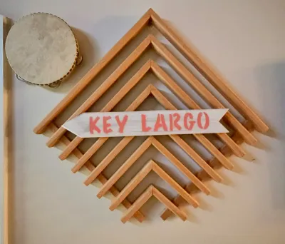 Geometric wooden chevron wall art featuring a white arrow sign with "KEY LARGO" in red lettering, shown alongside a small...