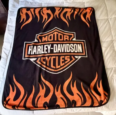 Harley-Davidson fleece throw blanket featuring the classic bar and shield logo with orange flame graphics on a black background.