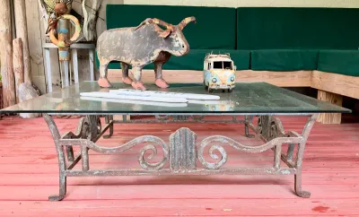 Wrought iron coffee table with a glass top, featuring scrollwork details and a weathered patina, styled with rustic metal decor.