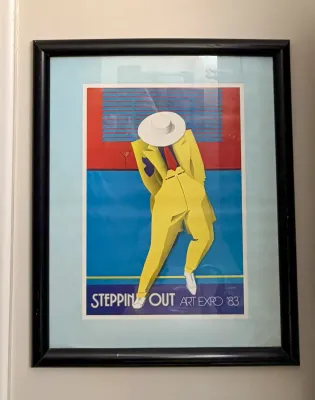 Framed "Steppin' Out Art Expo '83" exhibition poster featuring a stylized figure in a yellow suit, presented under...