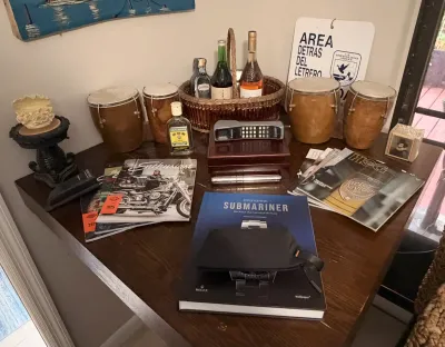 Eclectic tabletop display featuring vintage bongo drums, a basket of wine bottles, a retro brick cell phone, Harley-Davidson magazines,...