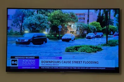 Samsung flat-screen television, wall-mounted and shown powered on displaying a news broadcast.