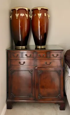 Pair of LP Caliente conga drums with a high-gloss wood finish and gold-tone hardware, displayed atop a traditional dark wood cabinet with...
