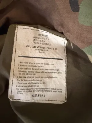 Interior label of a vintage US military M-65 cold weather field coat in size Large Regular, showing care instructions and stock number.
