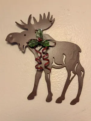 Rustic metal moose wall hanging featuring a festive holly and ribbon accent, suitable for holiday or cabin decor.