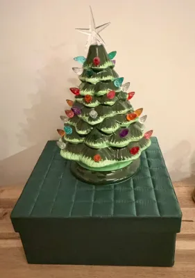 Vintage ceramic light-up Christmas tree with multi-colored plastic bulbs and a clear star topper, displayed on a green quilted box.