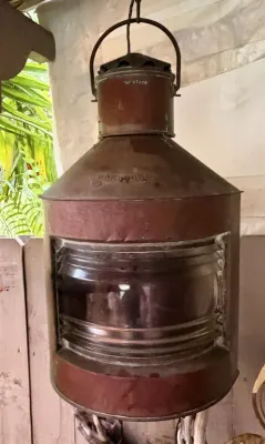 Vintage copper masthead ship lantern featuring a ribbed glass Fresnel lens and a weathered, rustic patina.