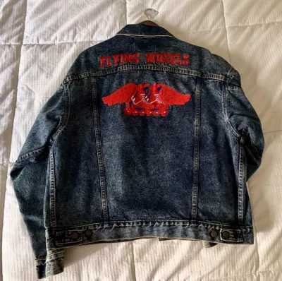 Vintage acid-wash denim jacket featuring a large embroidered back patch with the text "FLYING WHEELS" and a winged roller skate...