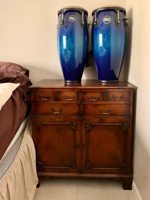 Pair of Meinl blue metallic conga drums resting on a traditional dark wood cabinet with brass hardware.