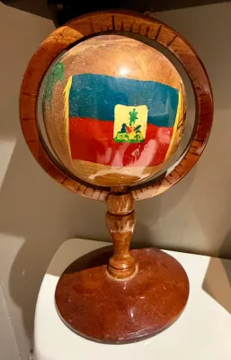 Hand-painted wooden globe featuring the flag of Haiti, mounted on a turned wood stand with a circular base.