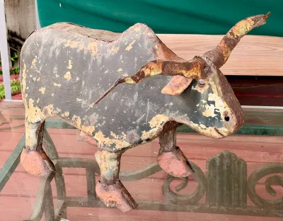 Rustic folk art metal bull sculpture with a heavily weathered, rusted, and peeling painted finish.