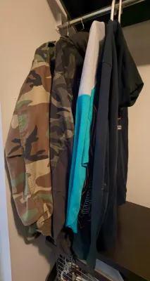 Selection of men's outerwear hanging in a closet, including a camouflage jacket, a dark zip-up hoodie, and a Harley-Davidson graphic...