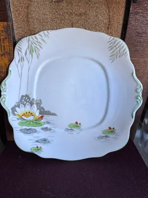Sale Photo Thumbnail #294: A vintage Roslyn China fine bone china square cake plate in the "Lily" pattern. Made in England, this piece features a scalloped edge with green trim, molded handles, and a hand-painted water lily pond scene with willow branches. Marked on the underside w
