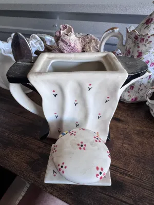 Sale Photo Thumbnail #178: A whimsical novelty ceramic teapot designed by Tony Carter, featuring a black cat with green eyes peeking out from under a draped white tablecloth. The lid is styled as a colorful striped and floral-patterned tea cozy or cake. Hand-painted details. Marked