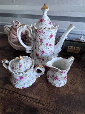 Sale Photo Thumbnail #98: A beautiful vintage 3-piece porcelain tea service set by Lefton China. This set features a delicate hand-painted pink rosebud and green leaf pattern on a white ground, accented with elegant gold-gilded trim and finials. 

Set includes:
- 1 Tall Teapot / C
