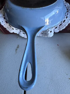 Sale Photo Thumbnail #263: A vintage Le Creuset No. 20 cast iron skillet featuring a light blue enameled exterior and handle. The underside is clearly stamped 'LE CREUSET MADE IN FRANCE 20'. The interior cooking surface shows significant wear, seasoning buildup, and discoloration f