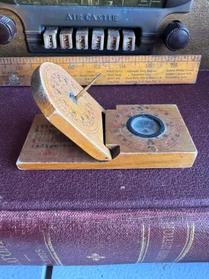 Sale Photo Thumbnail #54: An antique Chinese folding pocket sundial and compass (diptych style) crafted from wood. Features hand-painted Chinese characters, a central compass with a glass cover, and a folding metal gnomon on a hinged wooden plate. The underside and inner surfaces 