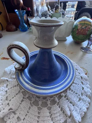 Sale Photo Thumbnail #336: A charming vintage ceramic chamberstick style candlestick holder featuring a finger loop handle. Decorated in a glazed blue and off-white color scheme with brown trim accents. Shows some light wear and minor glaze imperfections consistent with age and use
