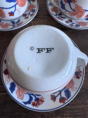 Sale Photo Thumbnail #62: A beautiful set of 5 vintage lidded tea cups with matching saucers by Fitz and Floyd. Each piece features a vibrant hand-decorated floral pattern in shades of blue, orange, and red. The bottoms are marked with the 'FF' copyright stamp, and one cup retains