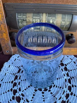 Sale Photo Thumbnail #249: A classic hand-blown drinking glass featuring a vibrant cobalt blue rim and a subtle light blue tint to the body. This rustic tumbler shows characteristic artisanal details, including small trapped air bubbles (seed bubbles) and a rough pontil scar on the