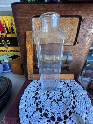 Sale Photo Thumbnail #254: A vintage clear glass jar featuring the embossed text "Ann's House of Nuts" on the bottom. The jar has a rectangular body tapering slightly towards the neck with a wide, rounded rim. It stands approximately 9.5 inches tall based on the adjacent ruler. Goo