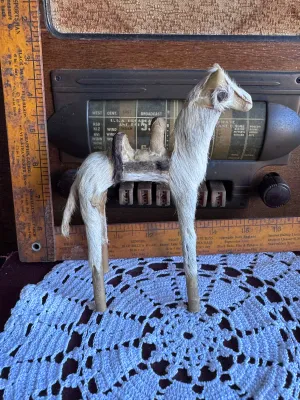 Sale Photo Thumbnail #184: A vintage handmade camel figurine covered in genuine animal fur with leather details forming the saddle and face. This folk art piece stands approximately 6 inches tall and features simple wooden dowel legs. Shows some age-related wear to the leather and 