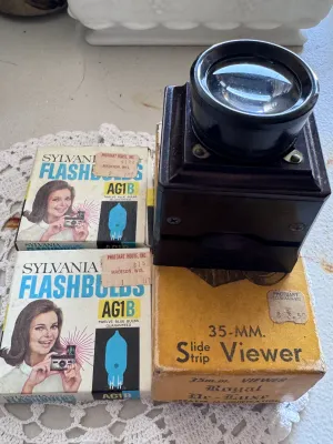 Sale Photo Thumbnail #312: Vintage photography lot featuring a Zarux 35mm Slide Strip Viewer (Royal De-Luxe model) made of dark bakelite/plastic, complete with its original cardboard box. The viewer is marked 'Zarux U.S.A.' on the bottom. Also included are two vintage boxes of Sylv