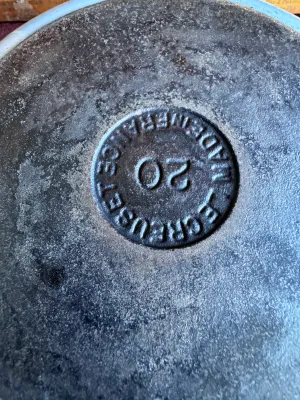Sale Photo Thumbnail #262: A vintage Le Creuset No. 20 cast iron skillet featuring a light blue enameled exterior and handle. The underside is clearly stamped 'LE CREUSET MADE IN FRANCE 20'. The interior cooking surface shows significant wear, seasoning buildup, and discoloration f