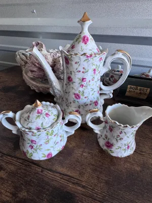 Sale Photo Thumbnail #97: A beautiful vintage 3-piece porcelain tea service set by Lefton China. This set features a delicate hand-painted pink rosebud and green leaf pattern on a white ground, accented with elegant gold-gilded trim and finials. 

Set includes:
- 1 Tall Teapot / C